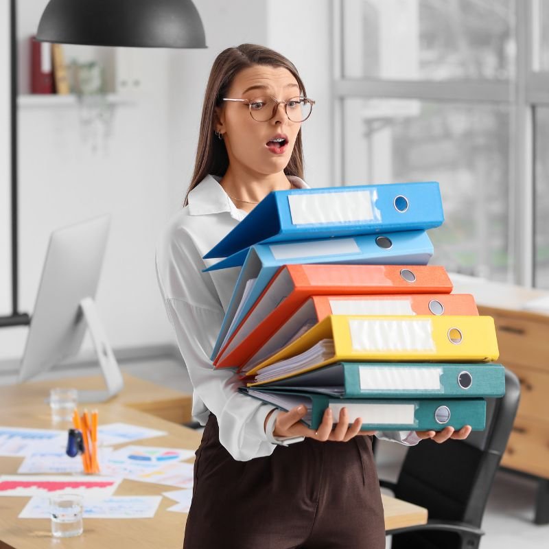 Female bookkeeper carrying a stack of colorful binders in the office